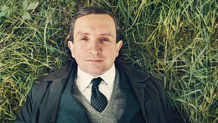John May (Eddie Marsan) lies on the grass looking upwards.