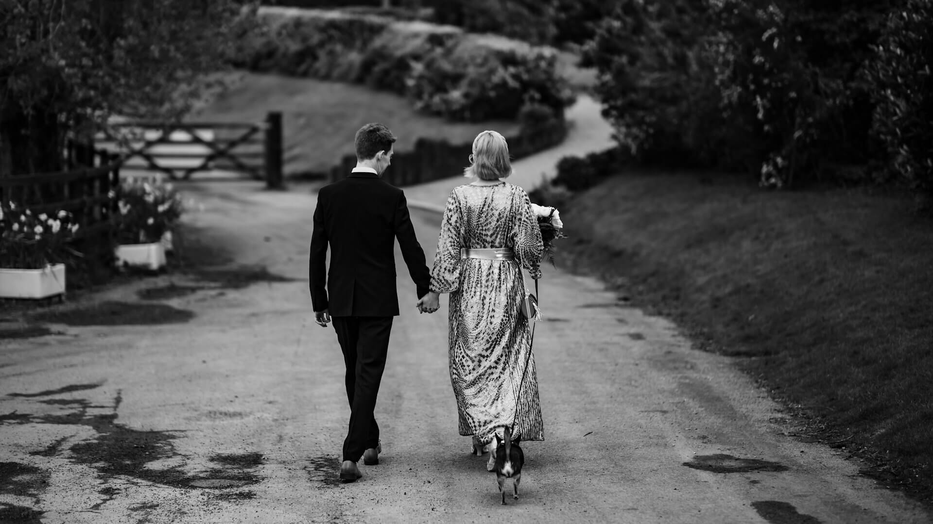 Husband, wife and dog walking down a lane away from camera